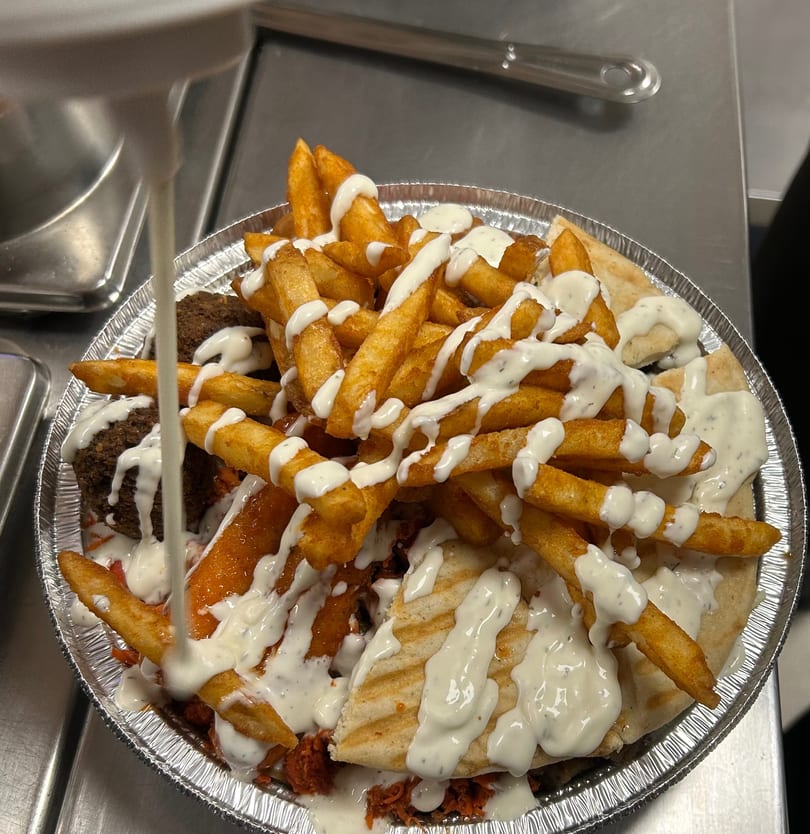 A platter of falafel, fries, and pita bread, generously drizzled with white sauce.