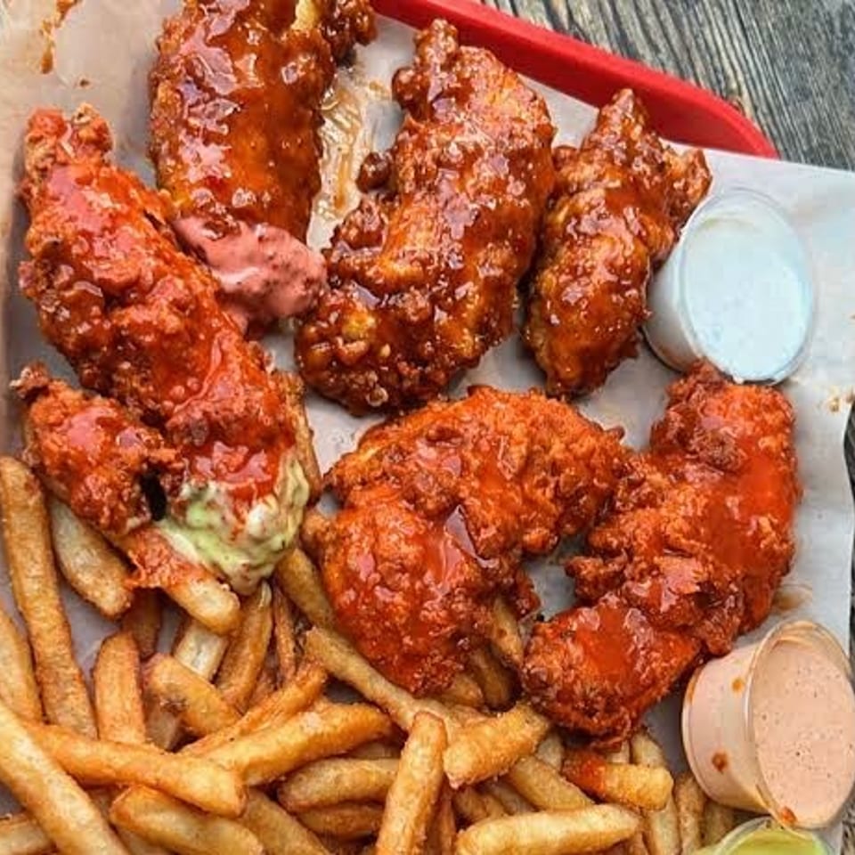 Close-up of a tray of crispy, saucy chicken tenders with fries and dipping sauces.