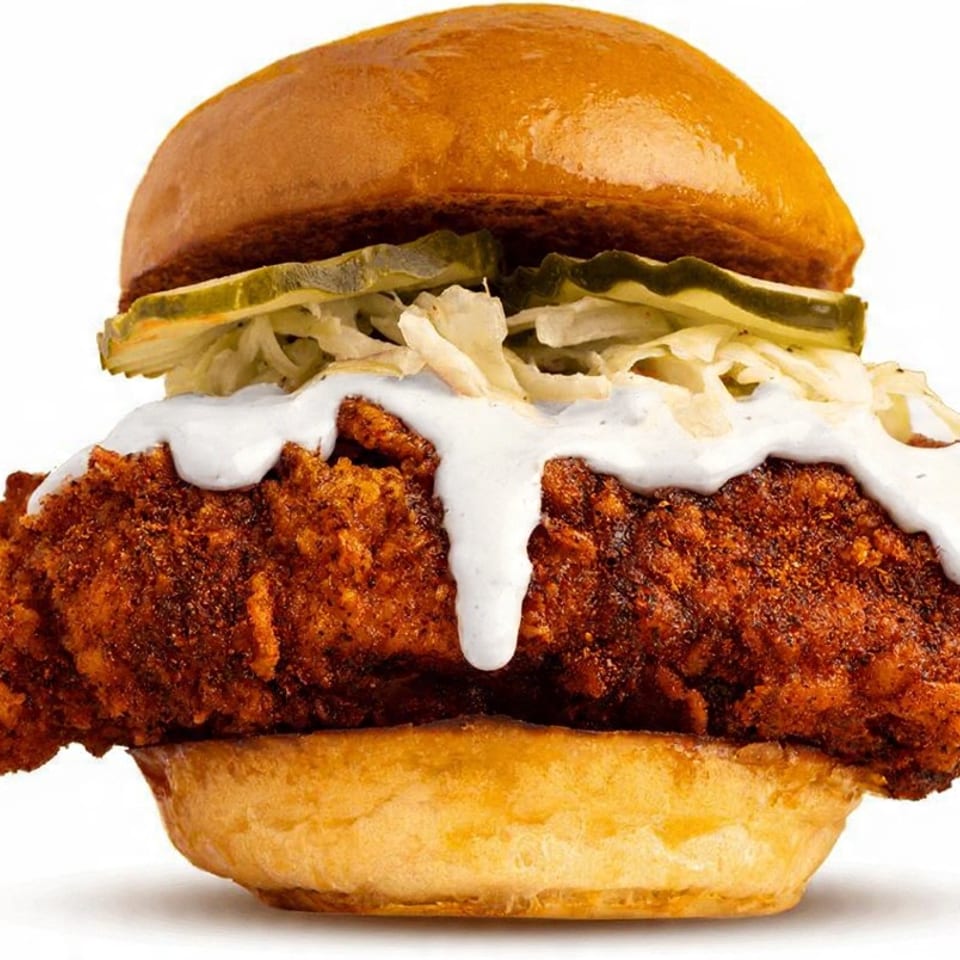 Crispy fried chicken sandwich with coleslaw, pickles, and white sauce on a brioche bun.