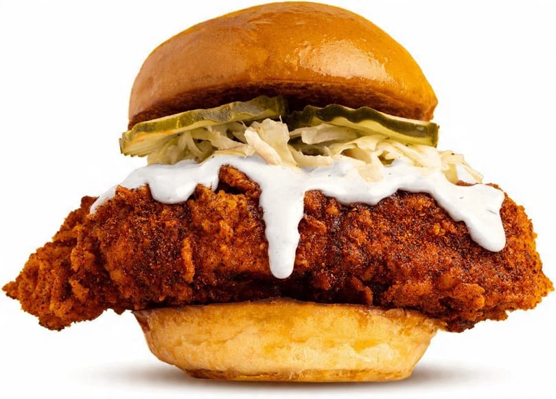 Crispy fried chicken sandwich with coleslaw, pickles, and white sauce on a brioche bun.