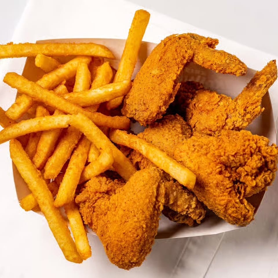 Crispy fried chicken wings and golden french fries in a paper container on a white napkin.