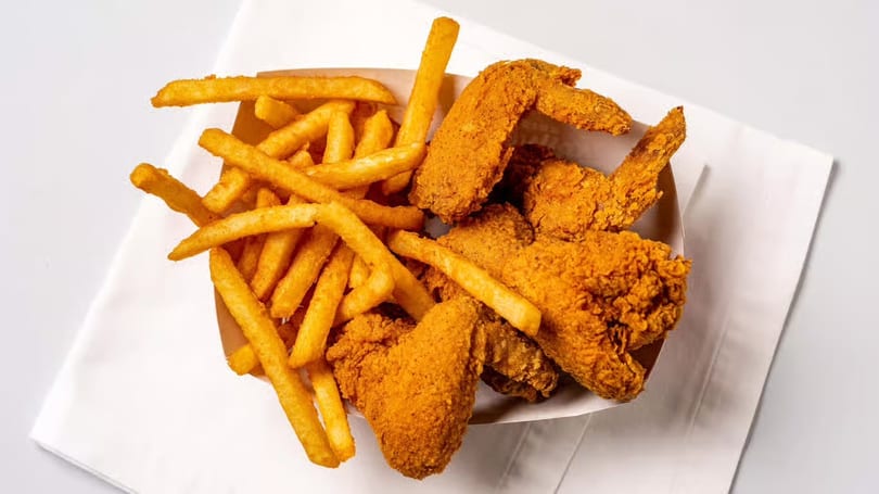 Crispy fried chicken wings and golden french fries in a paper container on a white napkin.