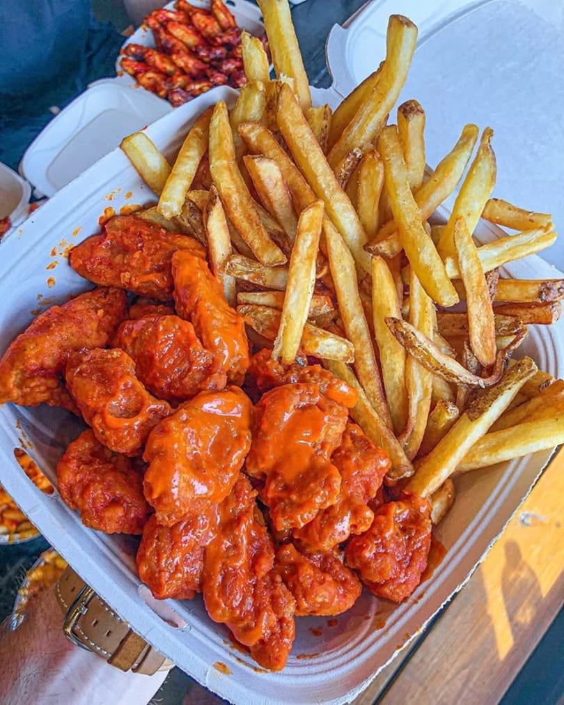 A takeout container filled with crispy french fries and saucy boneless buffalo wings.
