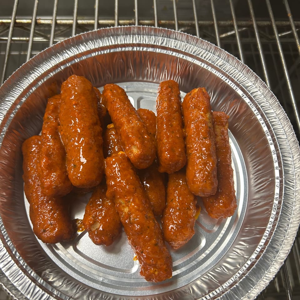 A foil container filled with numerous orange-red, sauce-covered mozzarella sticks on a metal rack.