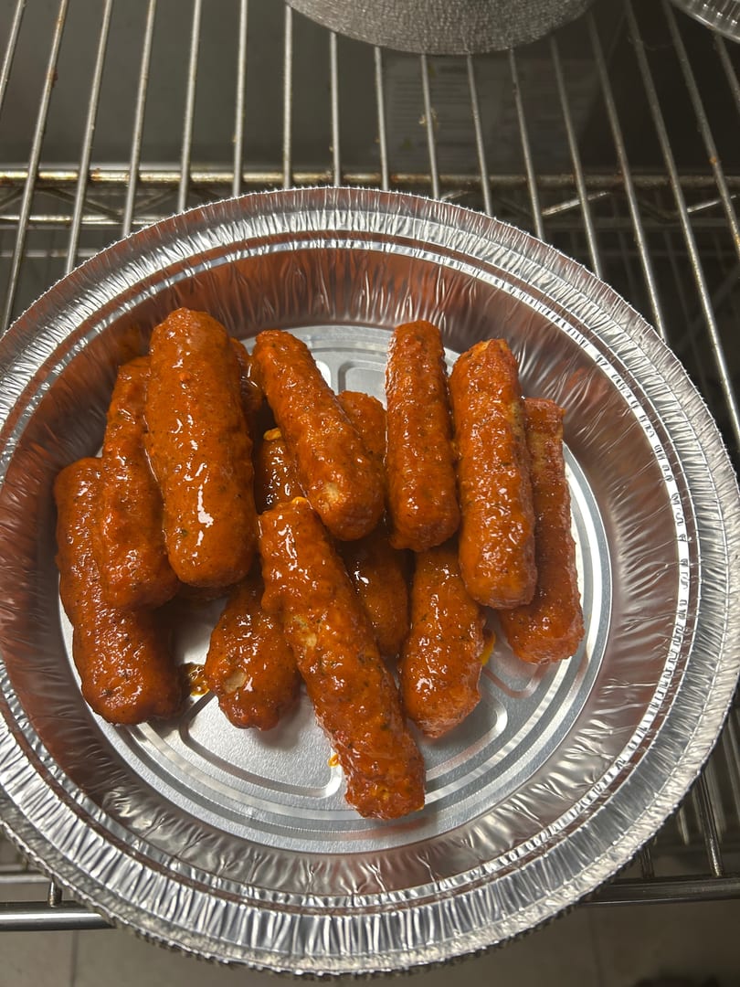 A foil container filled with numerous orange-red, sauce-covered mozzarella sticks on a metal rack.