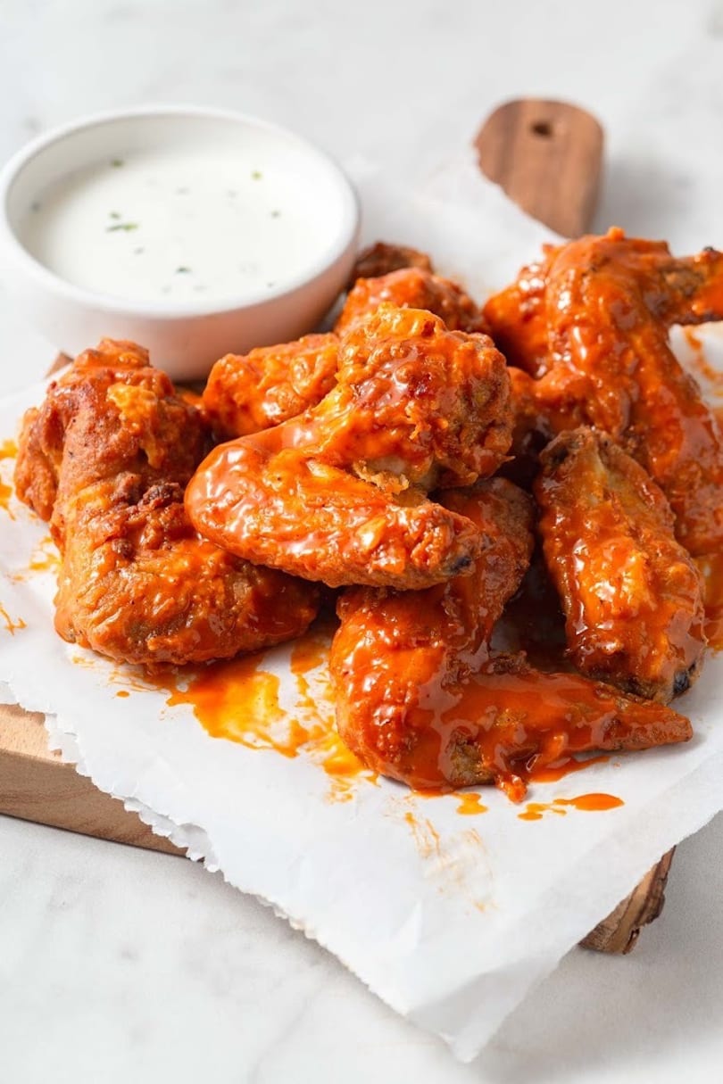 Buffalo wings coated in orange sauce, served on parchment paper with a side of ranch.