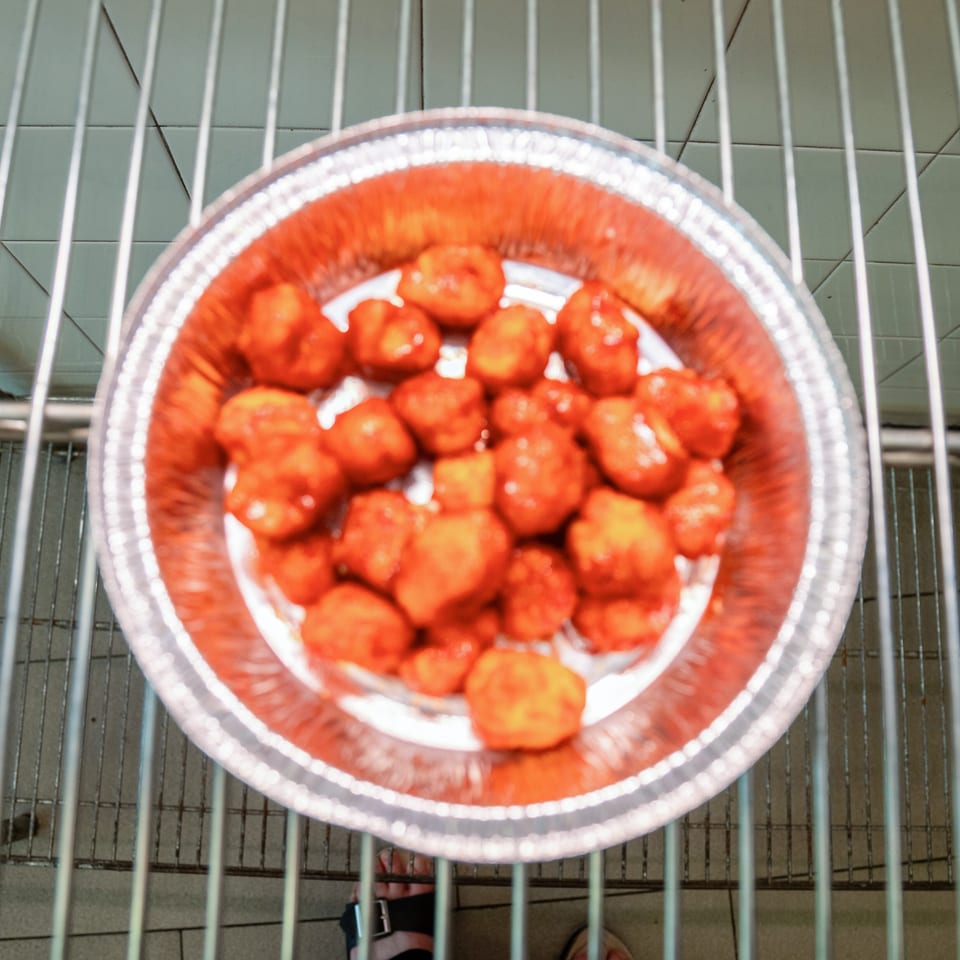 Overhead view of a foil pan filled with orange-red chicken pieces on a metal rack.