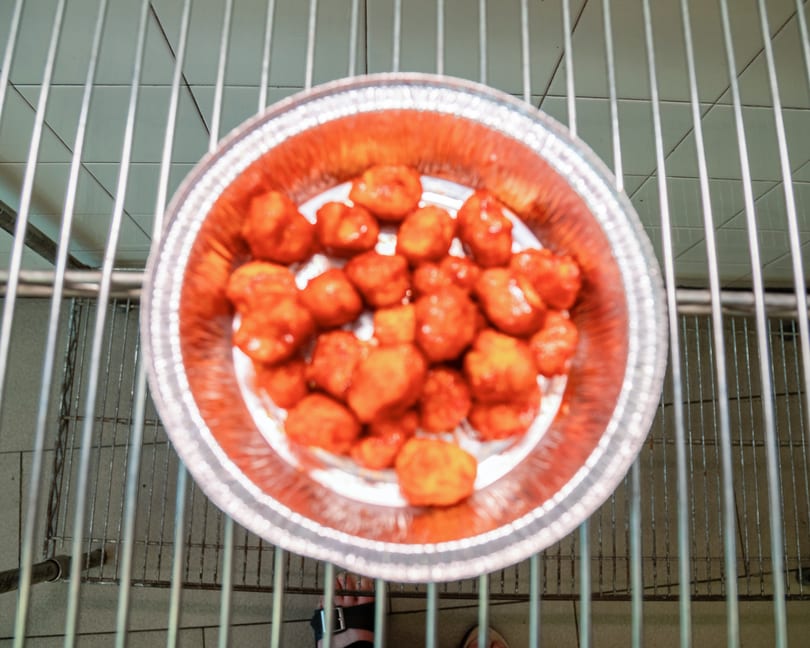 Overhead view of a foil pan filled with orange-red chicken pieces on a metal rack.
