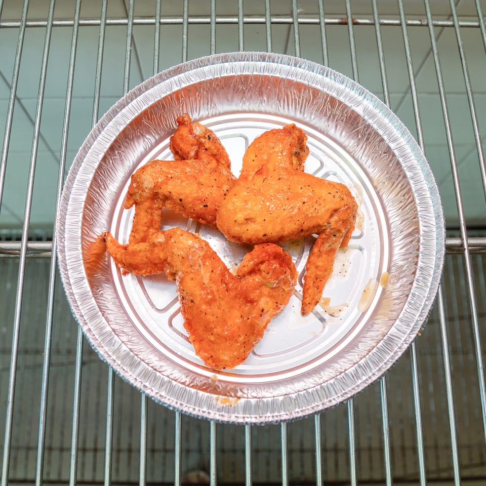 Three seasoned chicken wings in a round aluminum foil pan on a metal oven rack.