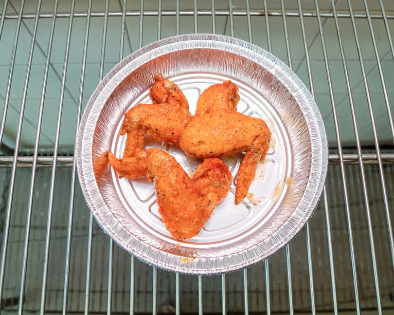 Three seasoned chicken wings in a round aluminum foil pan on a metal oven rack.