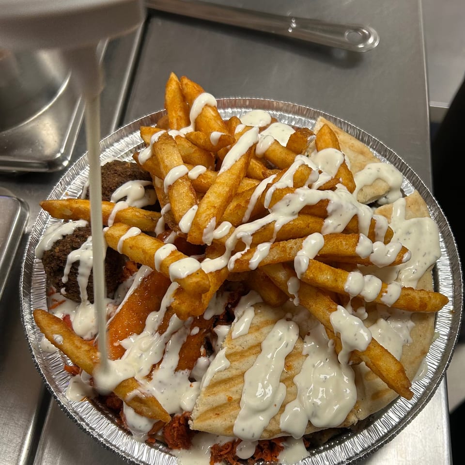 A platter of fries, falafel, and pita bread, generously drizzled with white sauce.