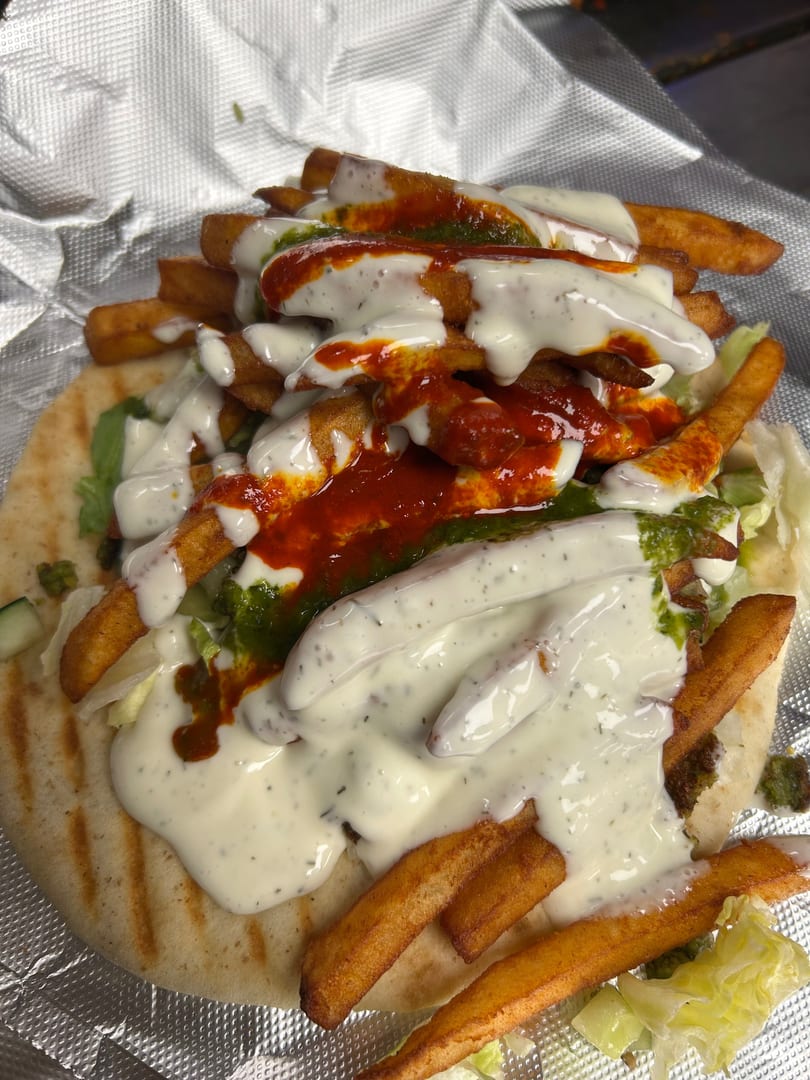 A pita bread topped with french fries, lettuce, white sauce, and red and green sauces.
