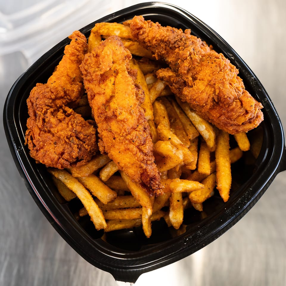 Crispy fried chicken tenders and seasoned french fries in a black takeout container.