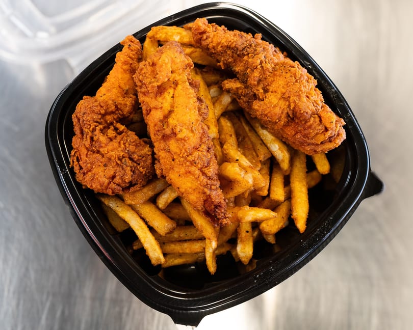 Crispy fried chicken tenders and seasoned french fries in a black takeout container.