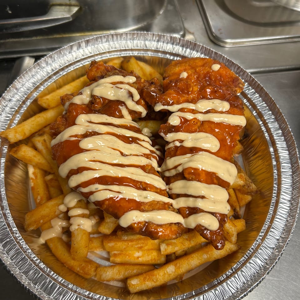 Two crispy chicken tenders drizzled with orange sauce and white dressing, served over golden fries in a foil container.