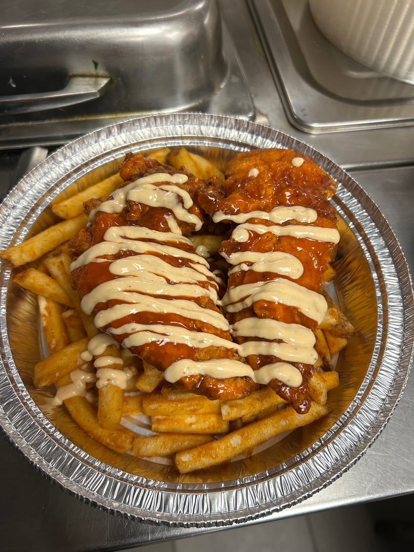 Two crispy chicken tenders drizzled with orange sauce and white dressing, served over golden fries in a foil container.