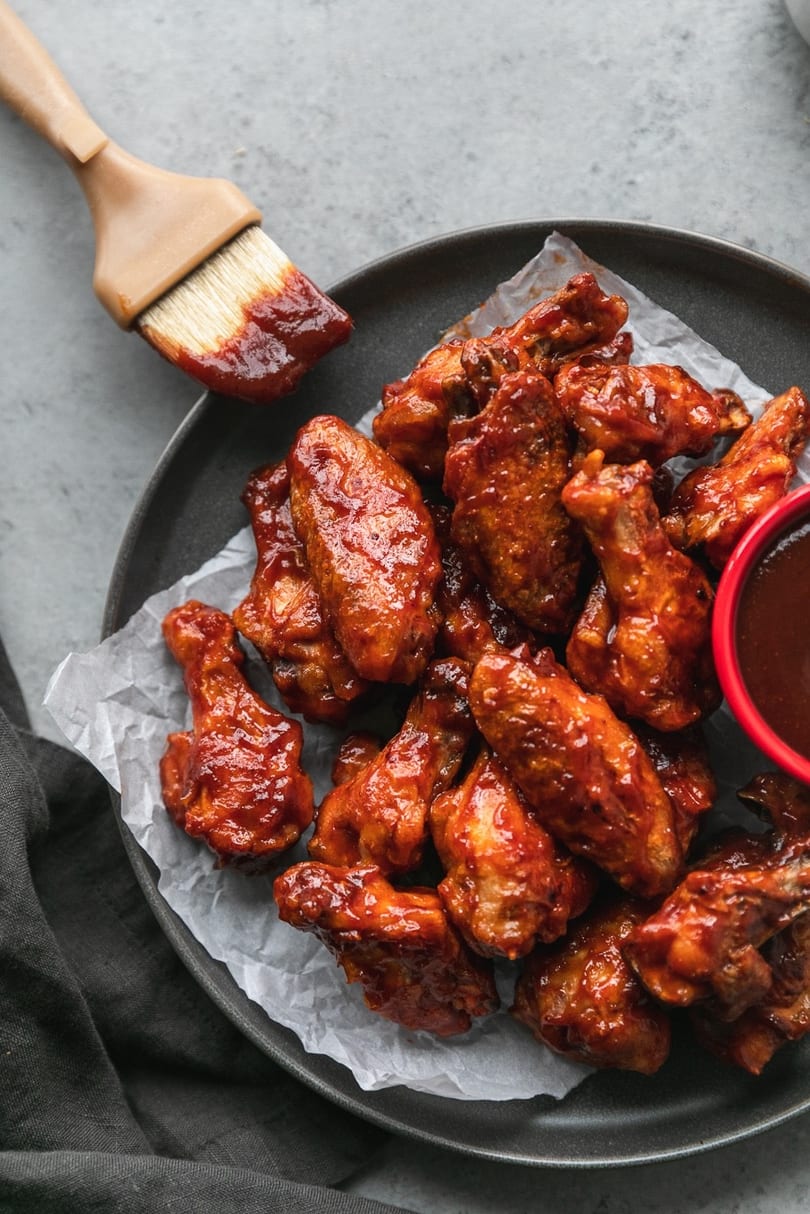 A plate of BBQ chicken wings with a basting brush and a side of sauce.
