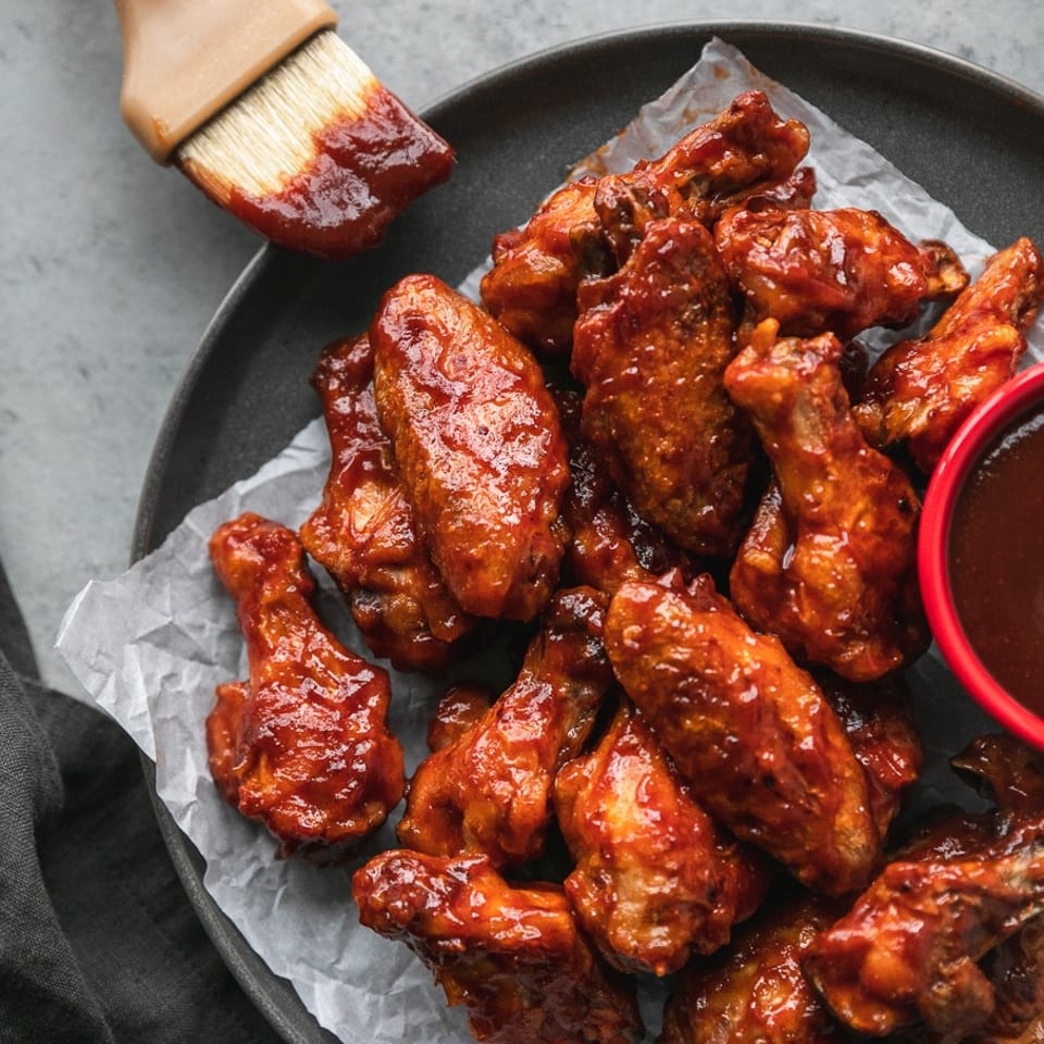A plate of BBQ chicken wings with a basting brush and a small bowl of sauce.