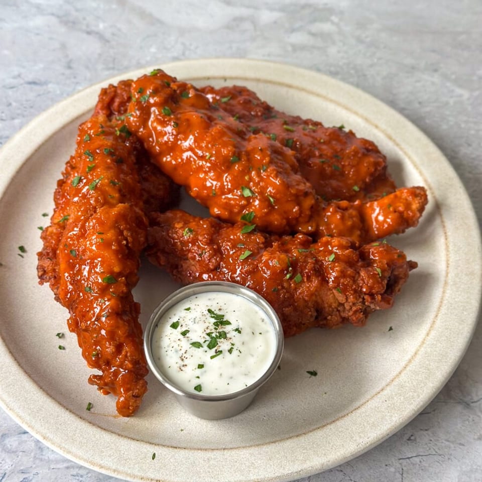 Crispy chicken tenders coated in a vibrant orange buffalo sauce with a side of ranch dressing.