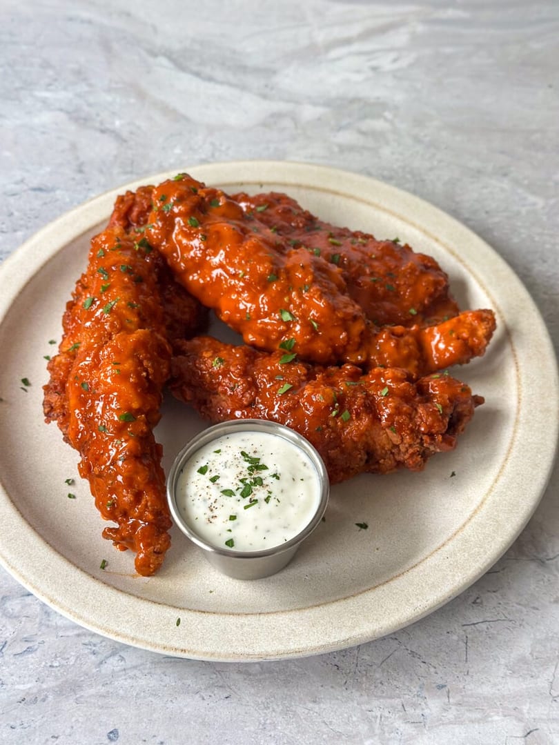 Crispy chicken tenders coated in a vibrant orange buffalo sauce with a side of ranch dressing.